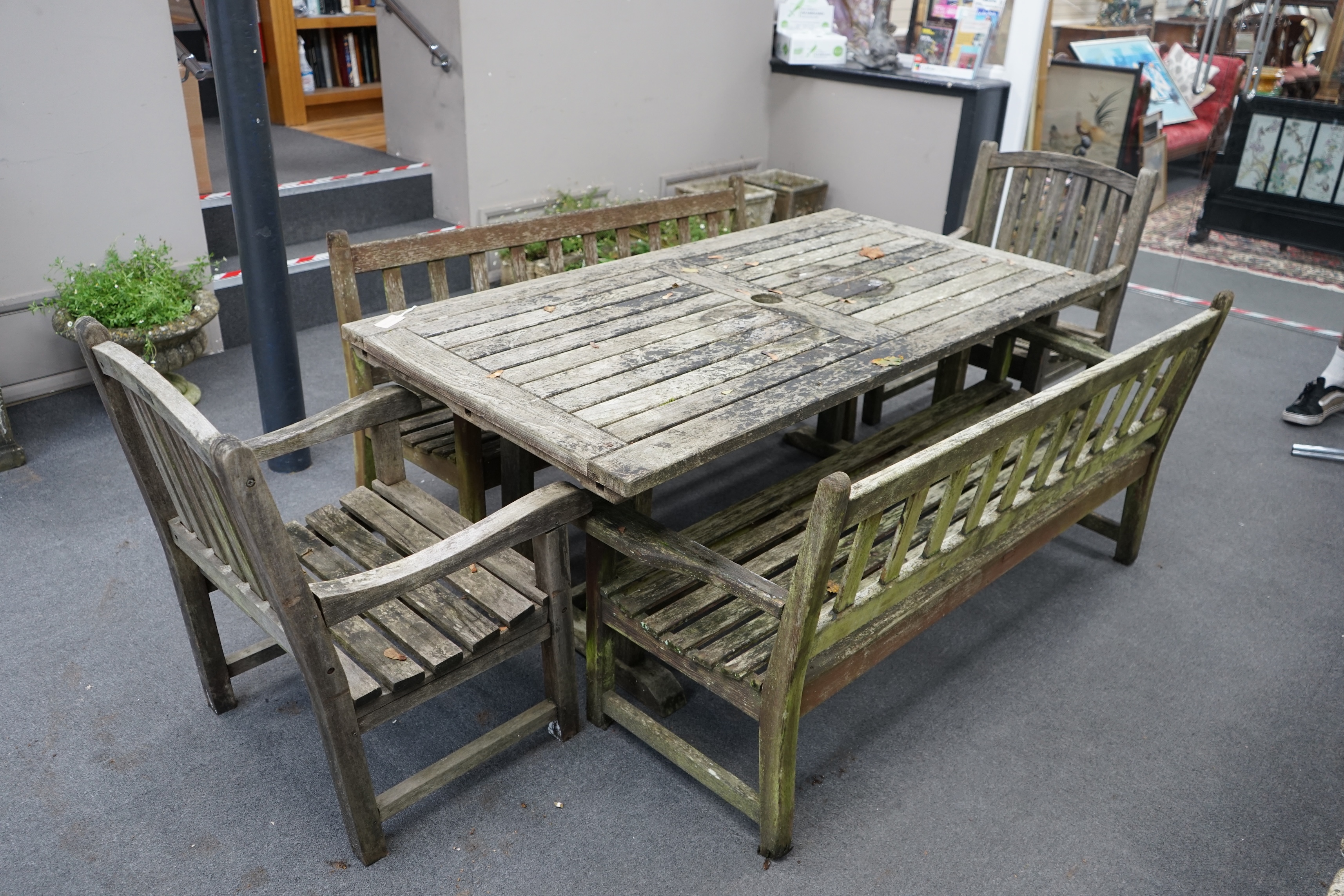 A weathered teak extending garden table, with pair of matching slatted benches and two elbow chairs